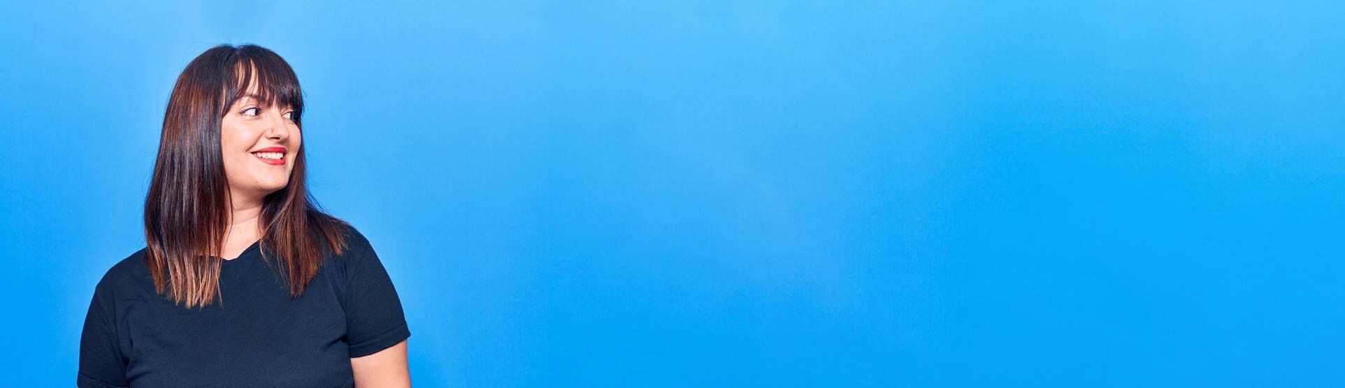 eine Frau in einem schwarzen Hemd und Jeans steht vor einem blauen Hintergrund