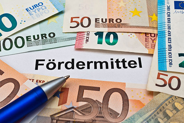 Verschiedene Euro-Banknoten und ein blauer Stift liegen auf einem Dokument mit der Überschrift "Fördermittel"