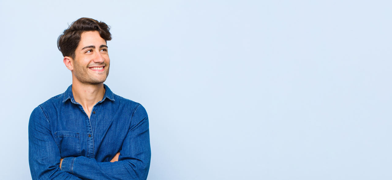 junger Mann lächelnd und mit gekreuzten Armen aufblickend