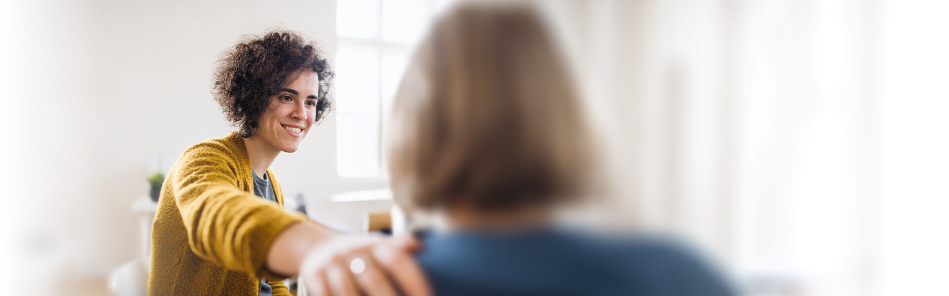 Weiblicher Coach legt im Coaching für Personen mit komplexen Ausgangslagen ihrer Kundin mitfühlend die Hand auf die Schulter.