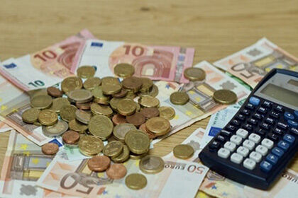 ein Haufen Geld in Scheinen und Münzen und ein Taschenrechner