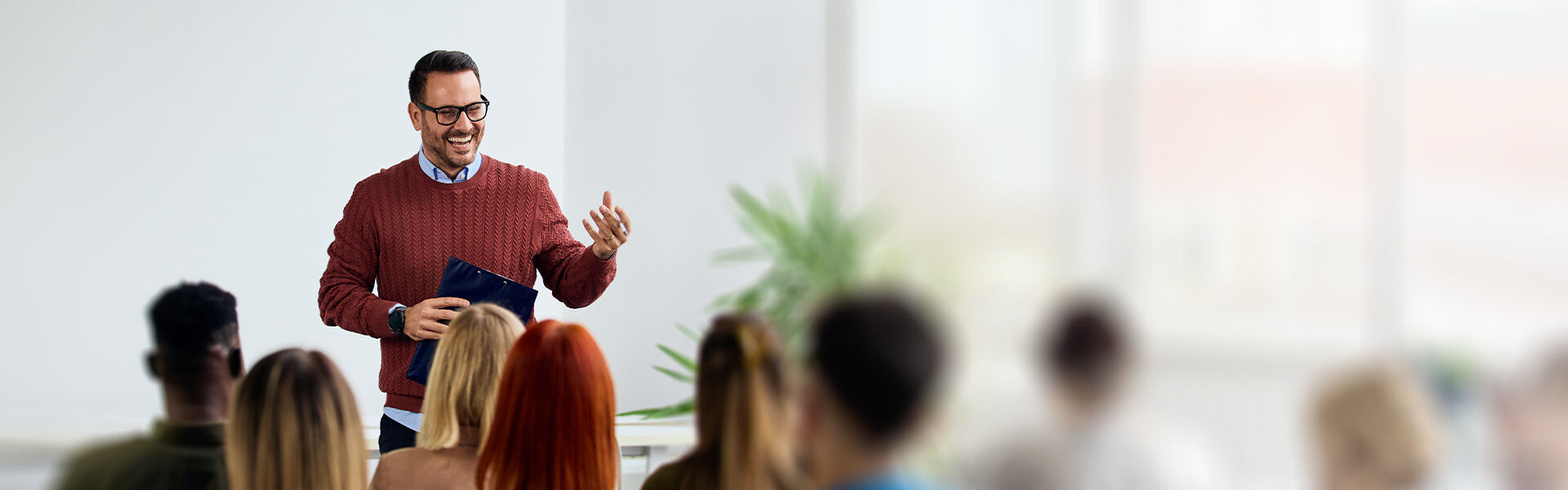 Ein Mann steht in einem Schulungsraum vor einer Gruppe Erwachsener und führt ein Coaching für Prüflinge durch.