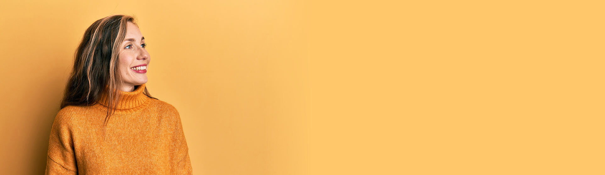 eine Frau in einem gelben Pullover, die gegen eine gelbe Wand steht